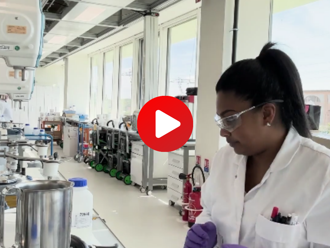 Une chercheuse en blouse blanche et gants violets travaillant dans un laboratoire L'Oréal R&I, illustrant un extrait de film marque employeur.